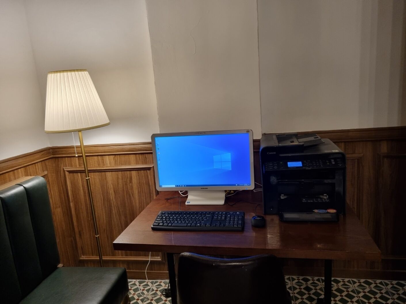 Une chambre d’hôtel avec un bureau en bois, un ordinateur de bureau, une imprimante, une lampe et un fauteuil en cuir noir.
