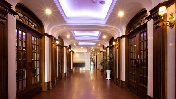 Een hotelgang met houten deuren, een gepoetste vloer en een plafond met ingebouwde verlichting.