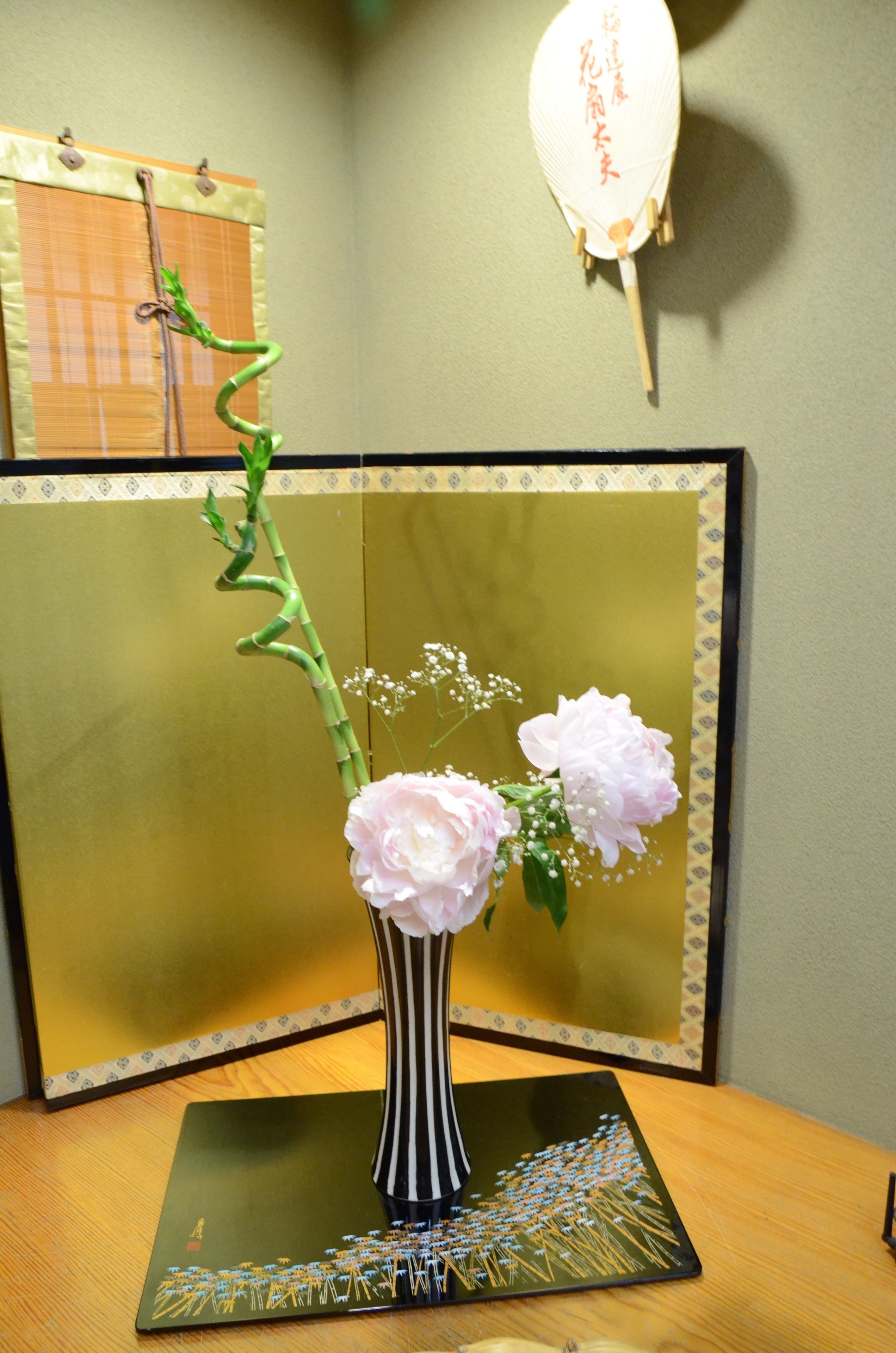 Una habitación con una mesa de madera, un florero blanco y negro a rayas con flores rosas, y un adorno en la pared.