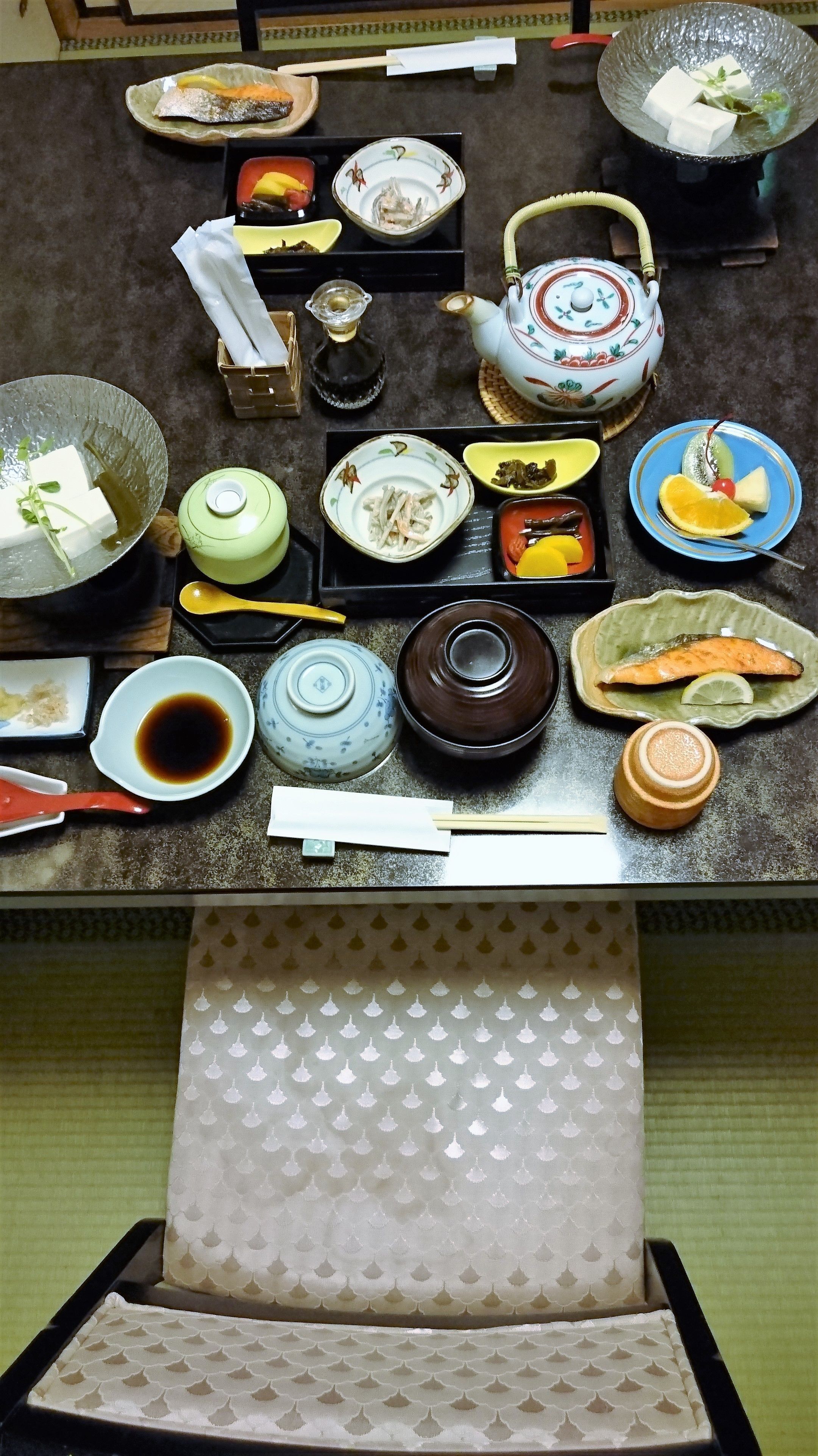 A dining table with various dishes, including fish, vegetables, and a teapot.