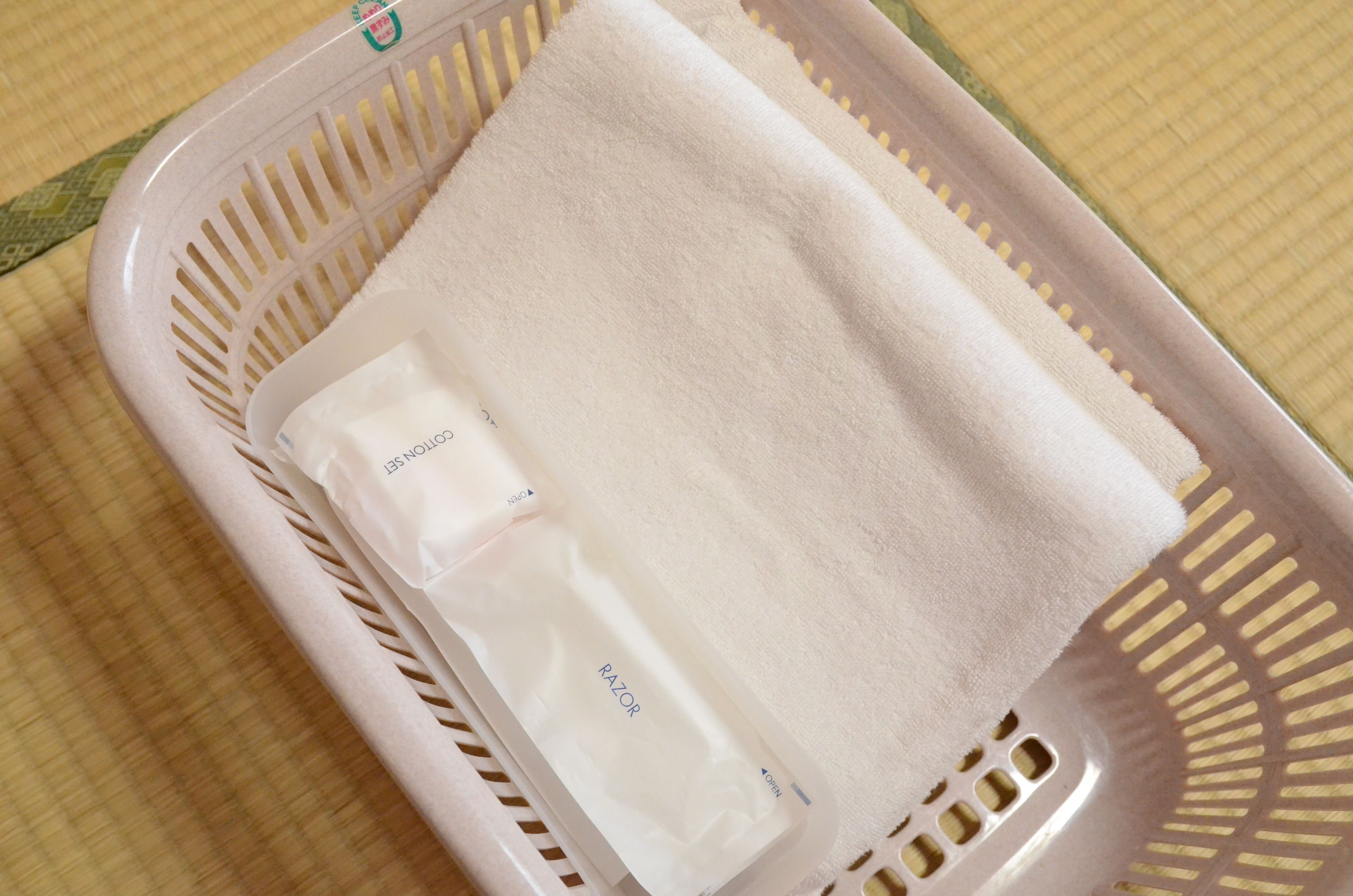 A white towel and a razor in a plastic basket on a textured surface.