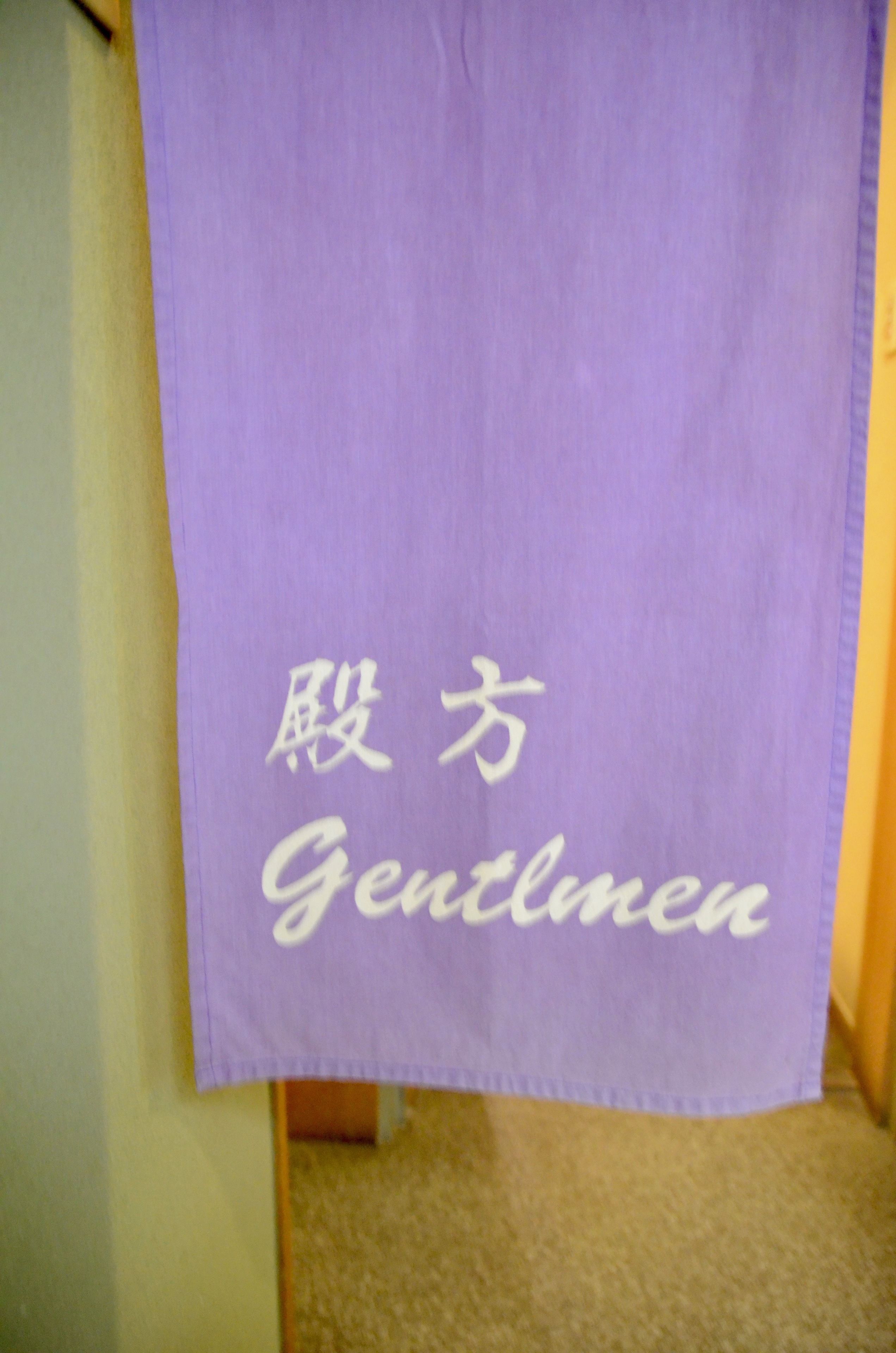 A purple towel hanging on a door with the word "Gentlemen" written on it.