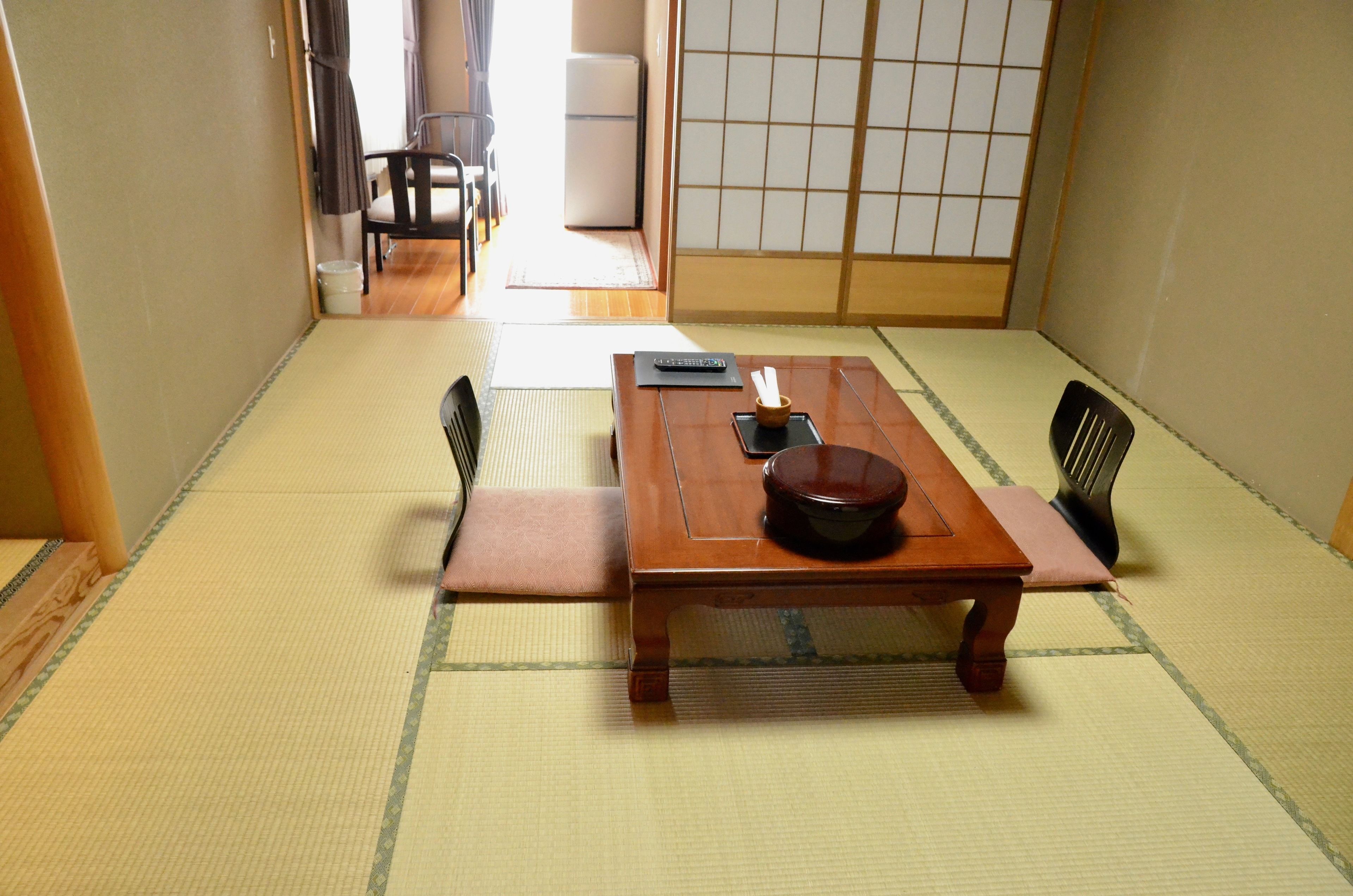 A traditional Japanese room with tatami flooring, a wooden table with a black bowl, and a sliding door with a grid pattern.