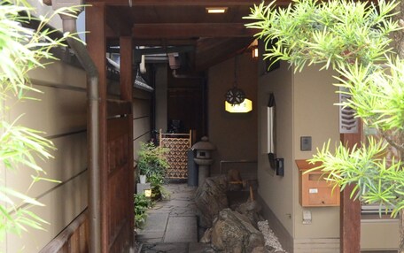 A traditional Japanese-style entrance with a tiled roof, stone pathway, and wooden structures.
