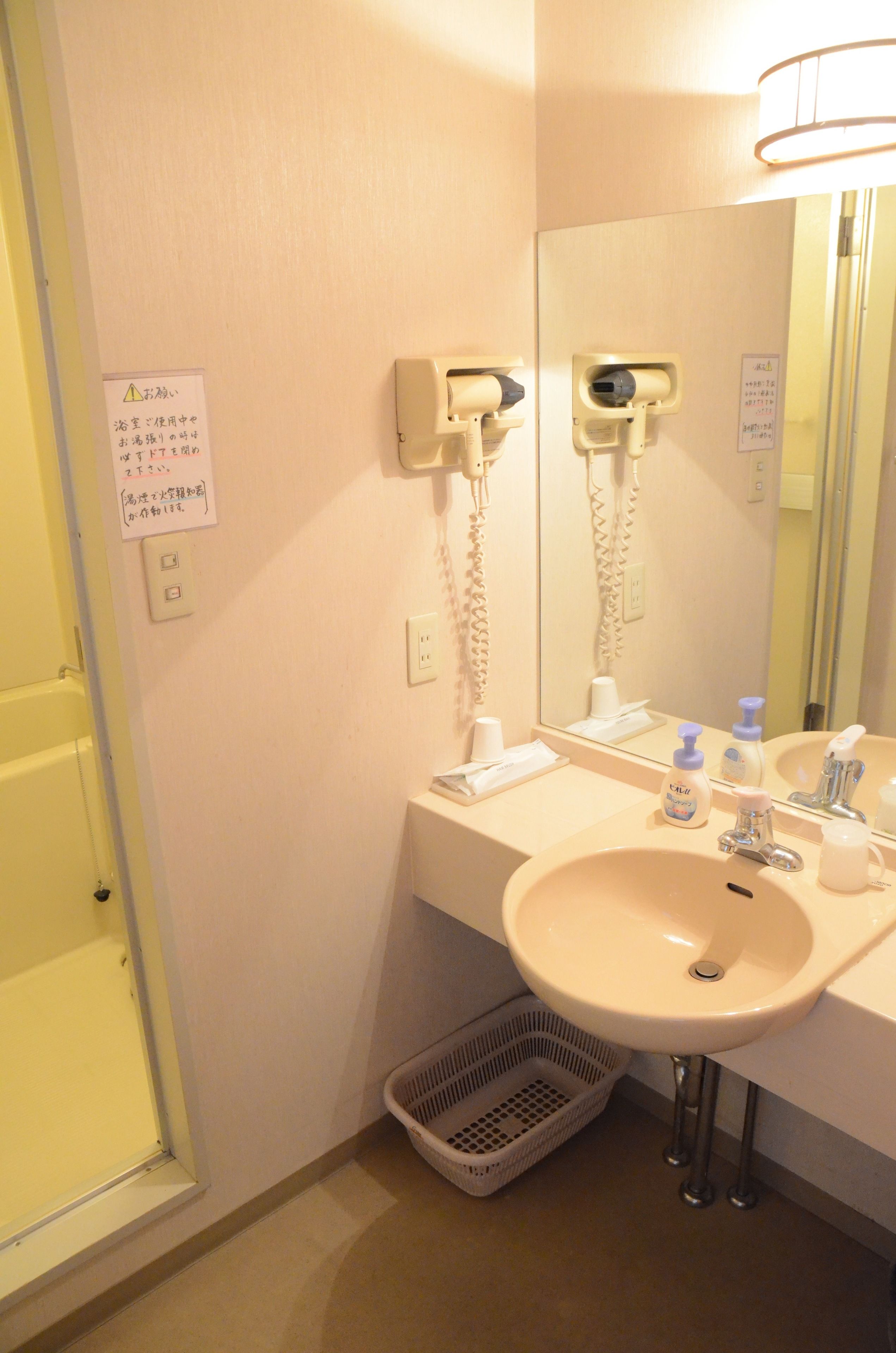 A bathroom with a sink, mirror, hairdryer, and a basket.