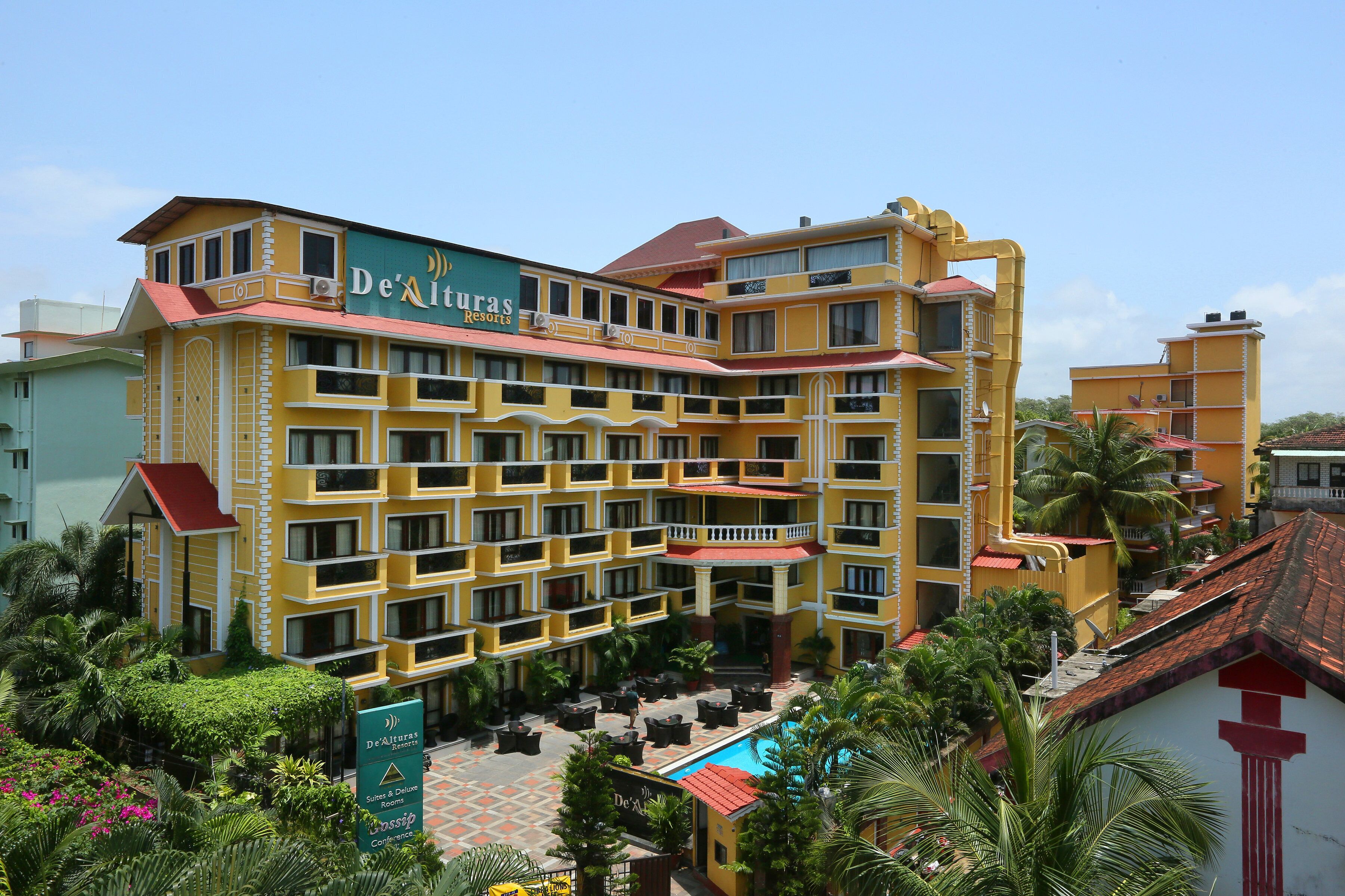 Un hotel de varios pisos con fachada amarilla, balcones y una piscina.