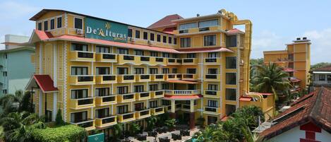 Un hotel de varios pisos con fachada amarilla, balcones y una piscina.