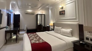 A hotel room with a large bed, a desk, a chair, a TV, and a ceiling fan. - De Alturas Resort (Candolim)