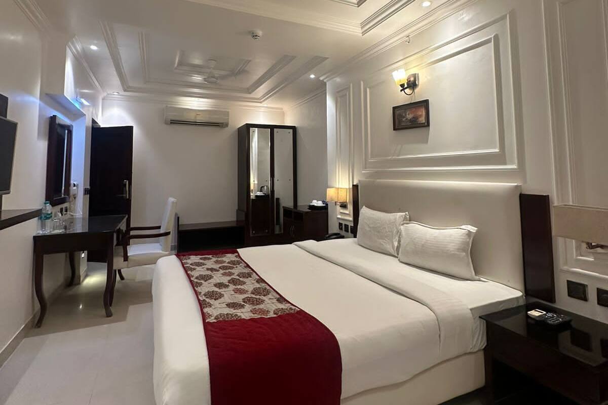 A hotel room with a large bed, a desk, a chair, a TV, and a ceiling fan.
