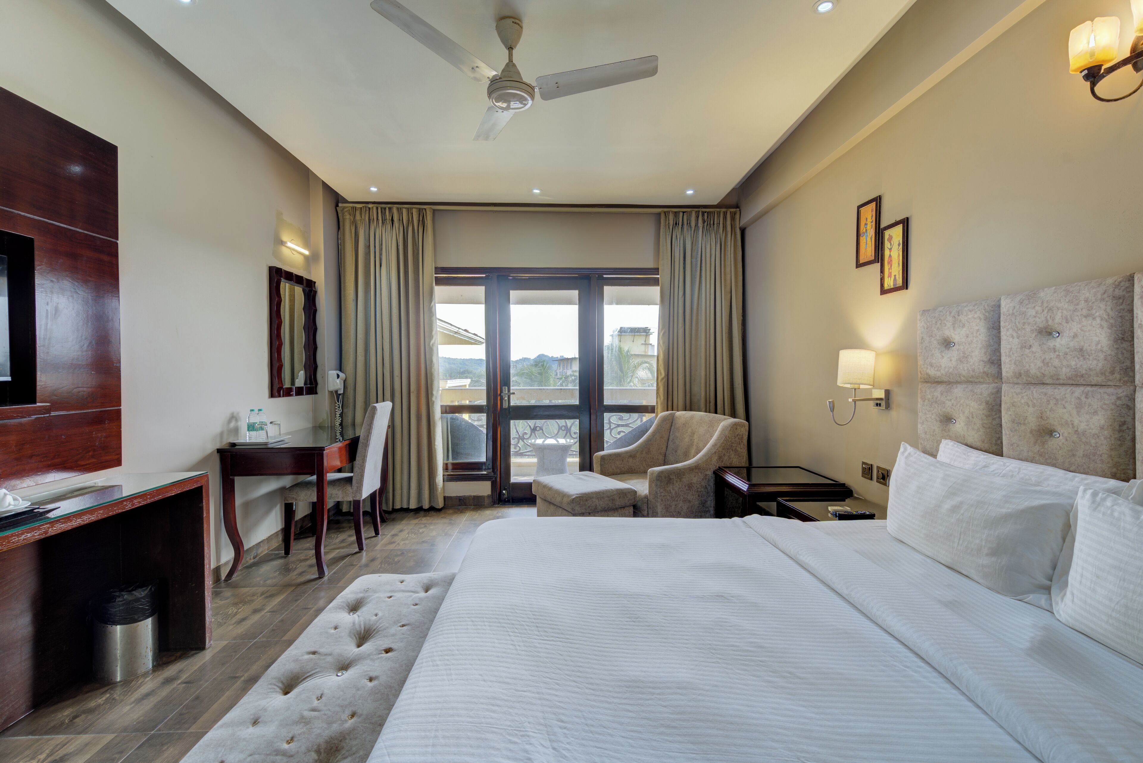 Ein Hotelzimmer mit einem großen Bett, einem Schreibtisch, einem Stuhl, einem kleinen Tisch und einem Deckenventilator.