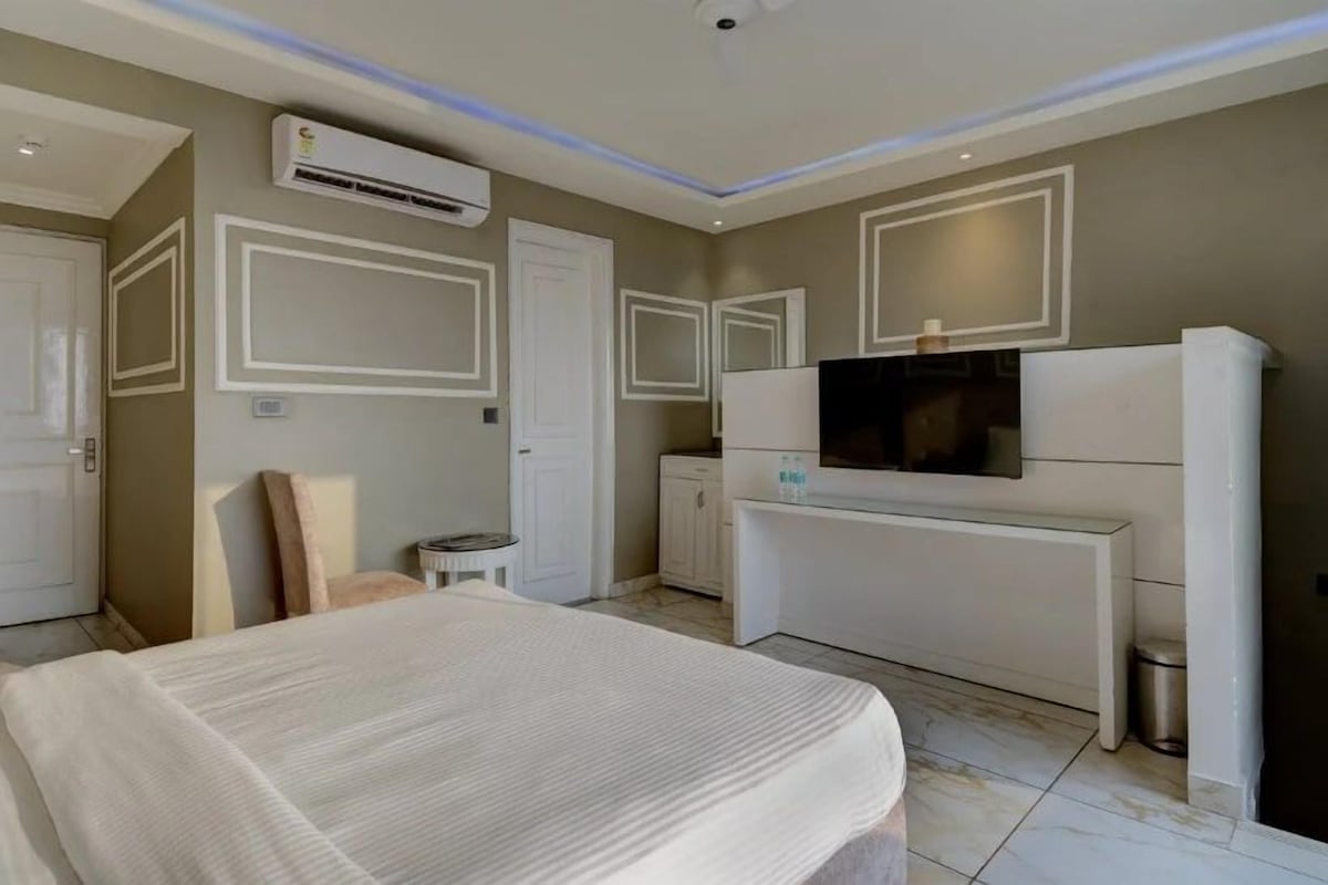 A bedroom with a bed, a TV, a desk, and an air conditioning unit.