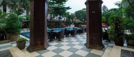 A checkered floor with a pool, outdoor seating, and palm trees.
