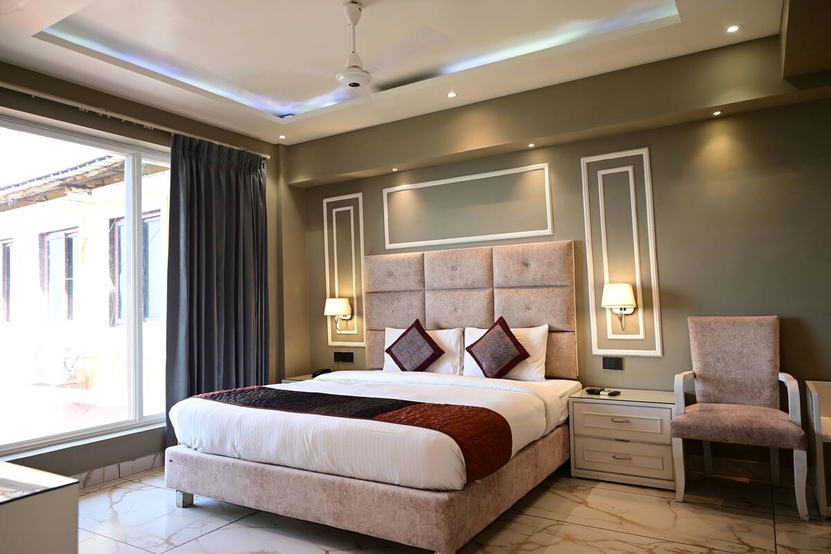 A modern bedroom with a large bed, bedside lamps, a chair, and a view of the outside.