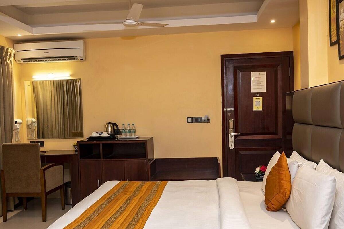 A hotel room with a bed, a desk, a chair, an air conditioning unit, and a door.