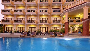 A hotel with a swimming pool, multiple balconies, and outdoor seating areas. - De Alturas Resort (Candolim)