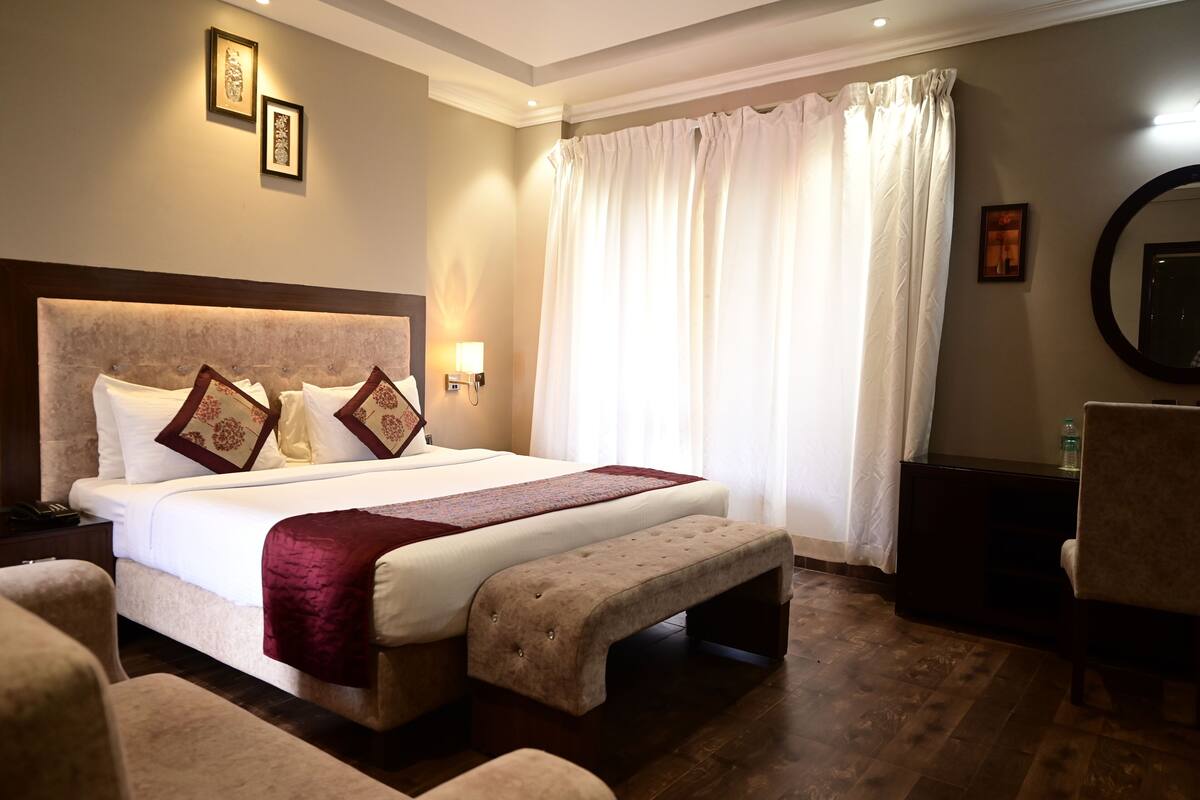 A hotel room with a large bed, a bench, a chair, a nightstand, and a mirror.