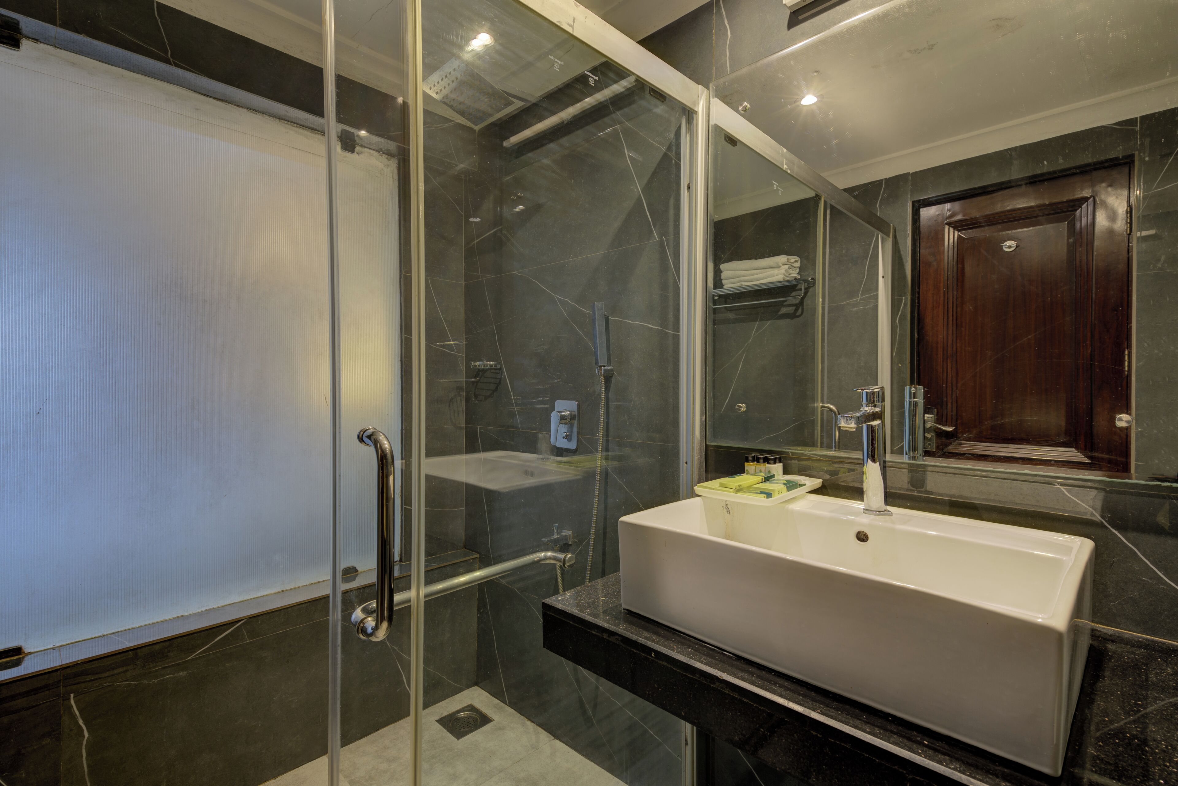 Un baño moderno con ducha envuelta en vidrio, un lavabo blanco y una encimera de mármol oscuro.
