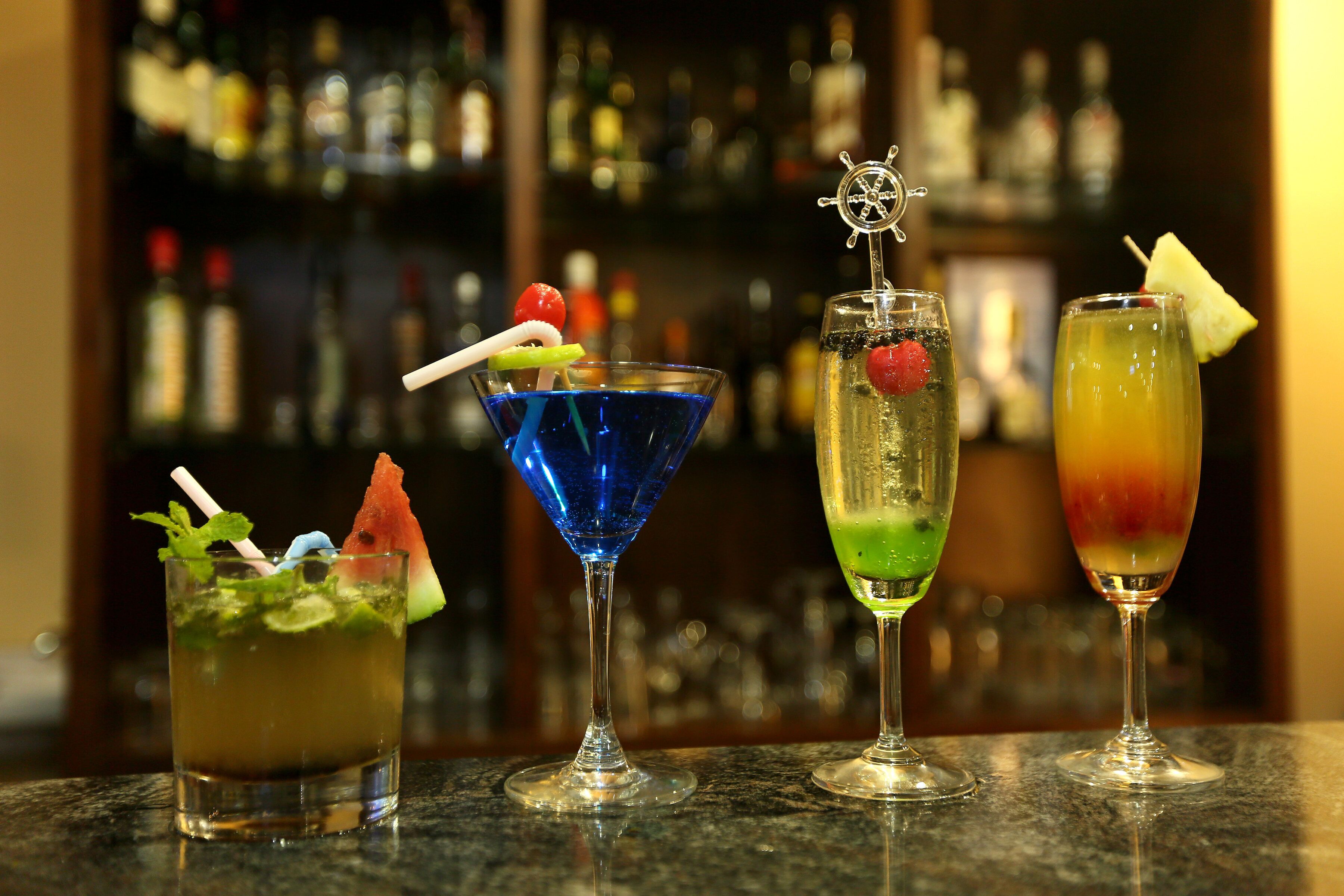 Trois cocktails sur le comptoir d’un bar, avec un arrière-plan flou composé de bouteilles.