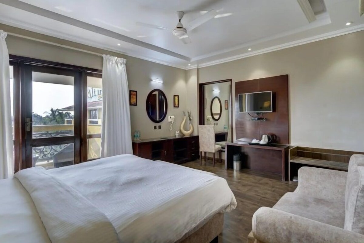 A hotel room with a bed, a desk, a chair, a TV, and a balcony with curtains.