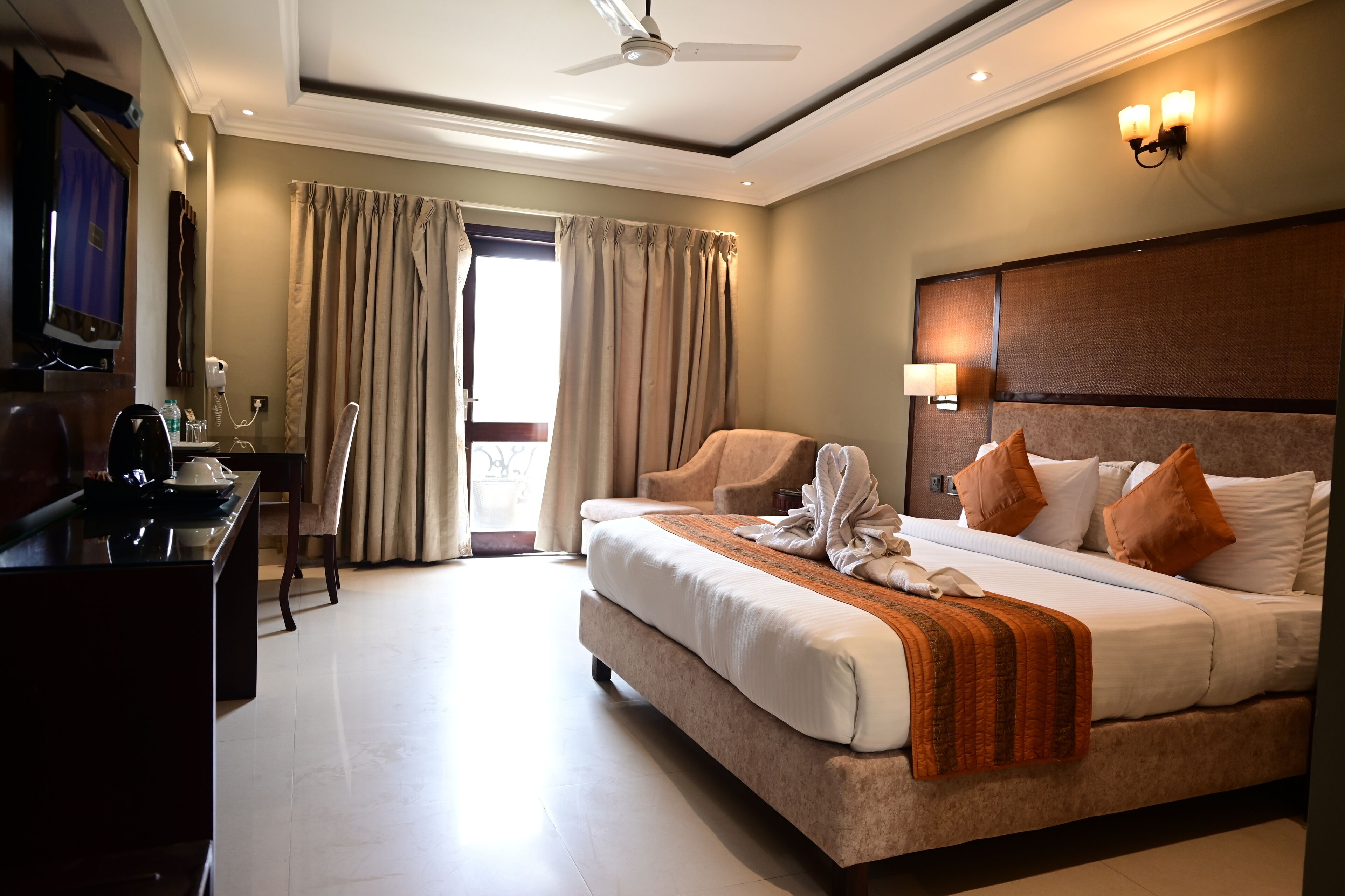 A hotel room with a large bed, a desk with a telephone, a chair, and a television.