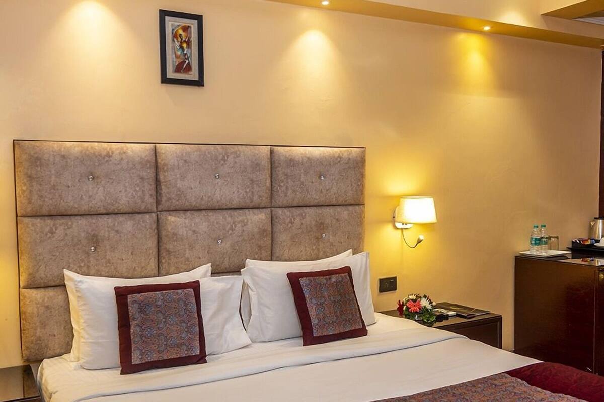 A hotel room with a large bed, a headboard, a nightstand, a lamp, and a framed picture on the wall.