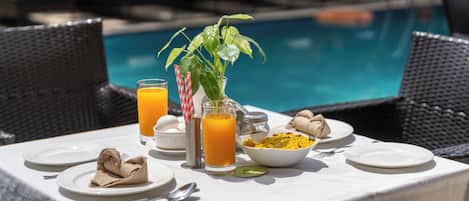 Una mesa de desayuno con platos, cubiertos, un tazón de cereal, un vaso de jugo de naranja y una planta en maceta.