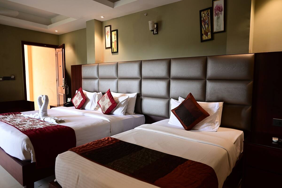 A hotel room with two beds, a large padded headboard, and artwork on the walls.