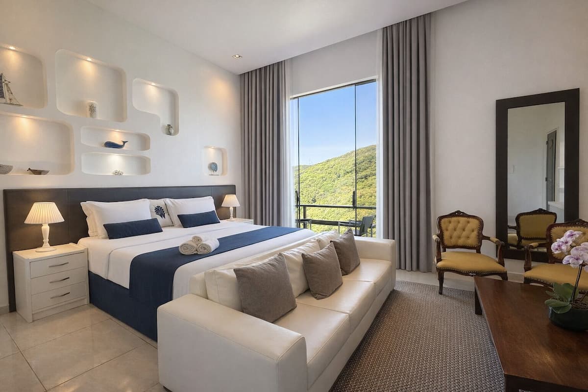 Une chambre d’hôtel moderne dotée d’un grand lit, d’un canapé, d’une table à manger et d’un balcon offrant une vue sur les collines.