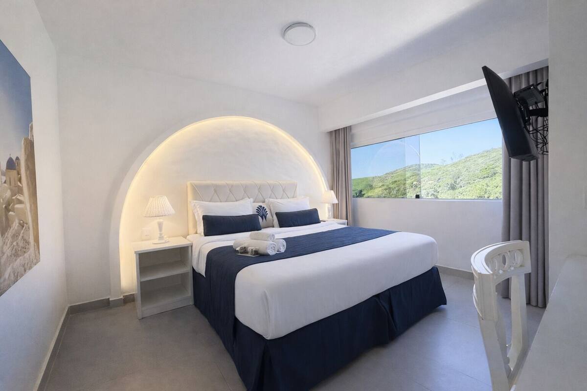 Une chambre d’hôtel avec un lit, une table de chevet, une télévision, une fenêtre donnant sur un beau paysage et un tableau au mur.