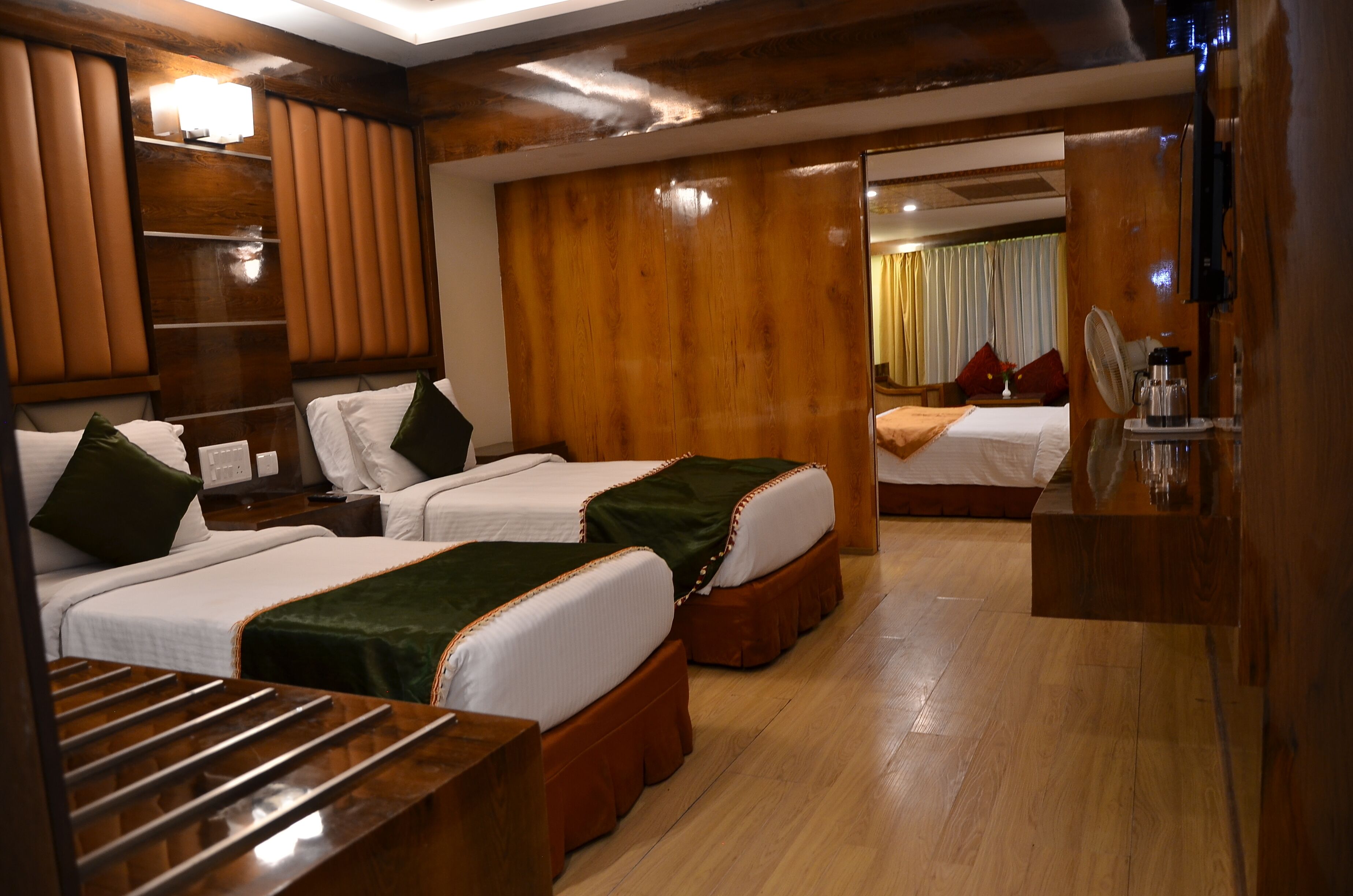 Hotelkamer met twee bedden, houten hoofdborden, een houten dressoir en een klein tafeltje met waterkoker en beker.