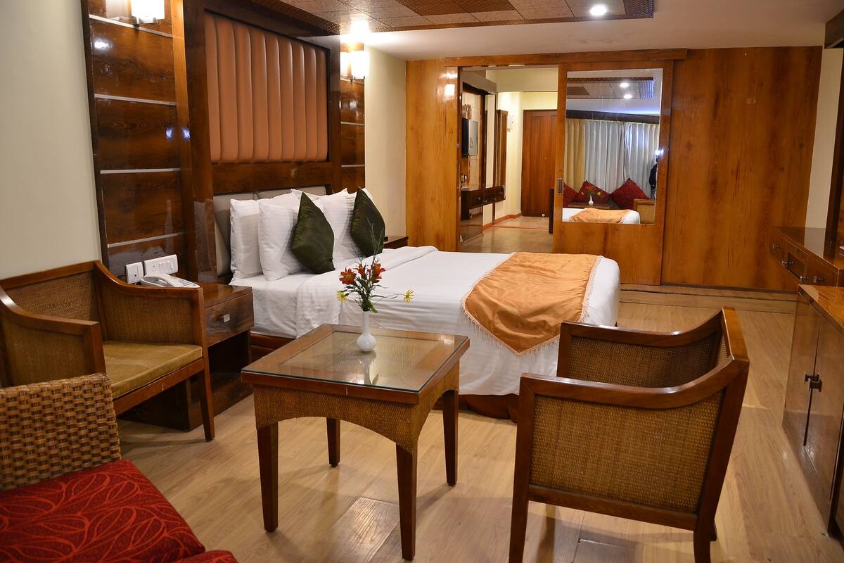 Habitación de hotel con cama, zona de estar con mesa y sillas, espejo y armario.