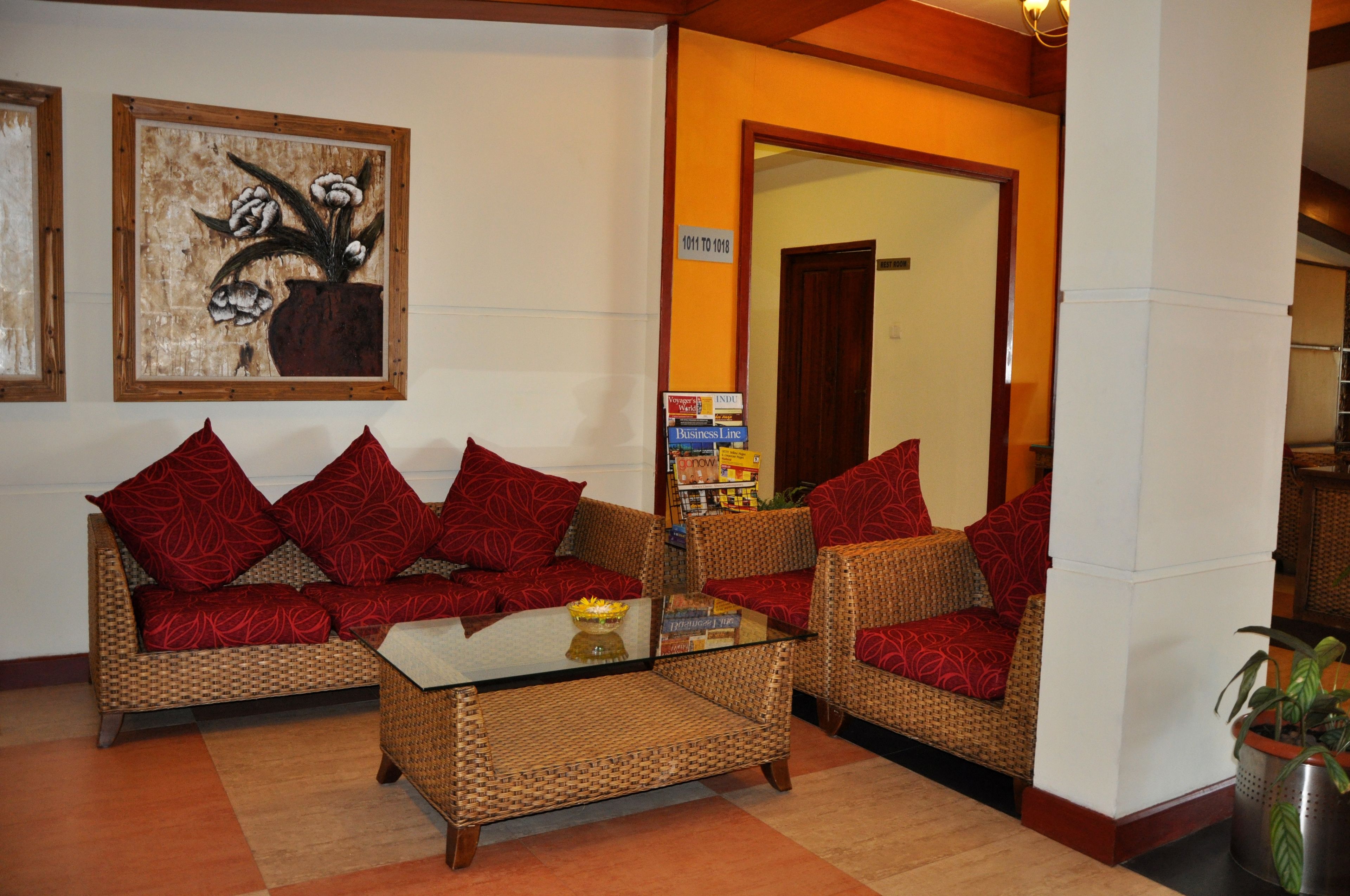 A lobby with wicker furniture, red cushions, a glass coffee table, and a framed artwork on the wall.