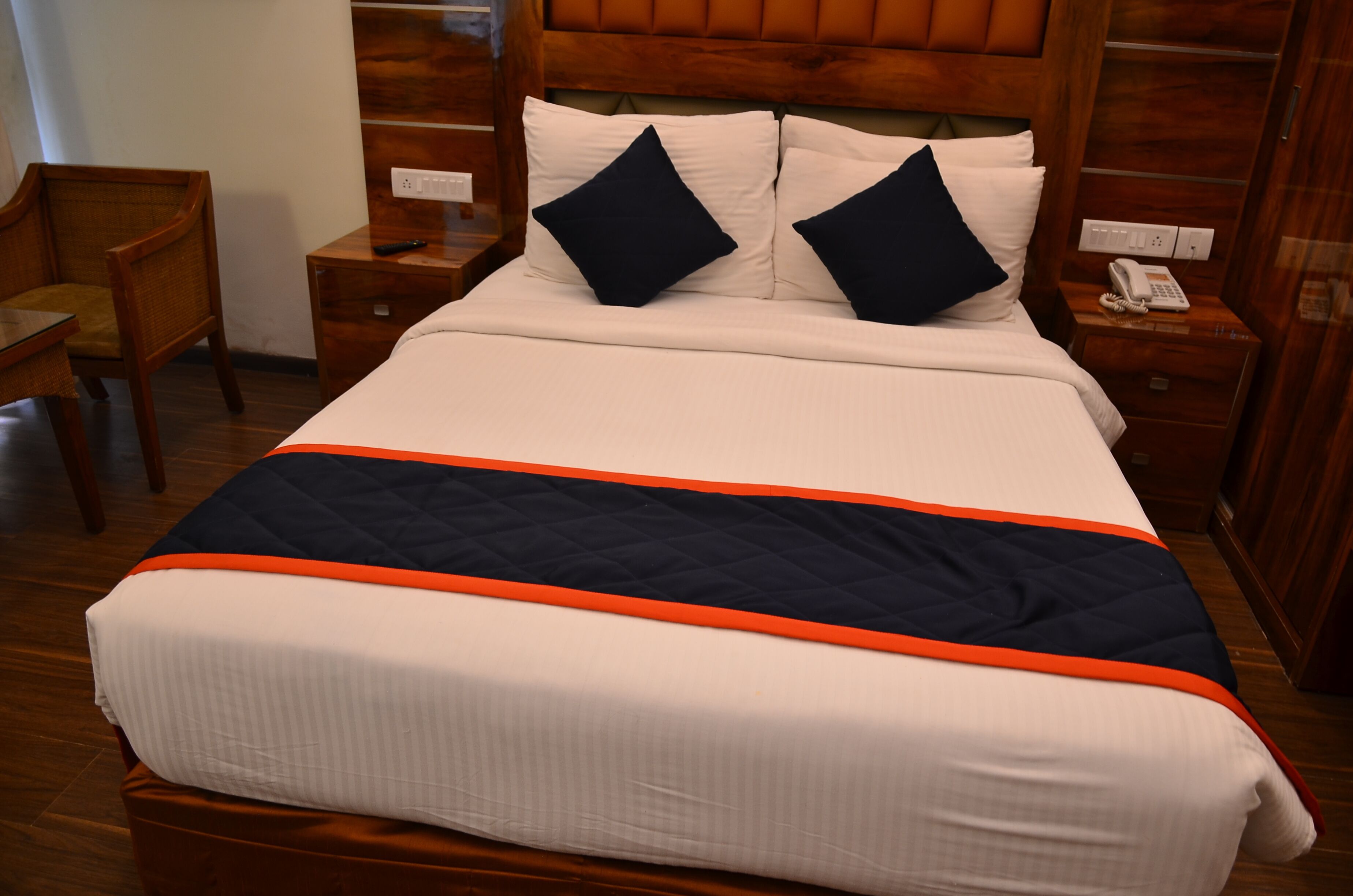 A hotel room with a large bed, wooden headboard, bedside tables with lamps, and a chair.