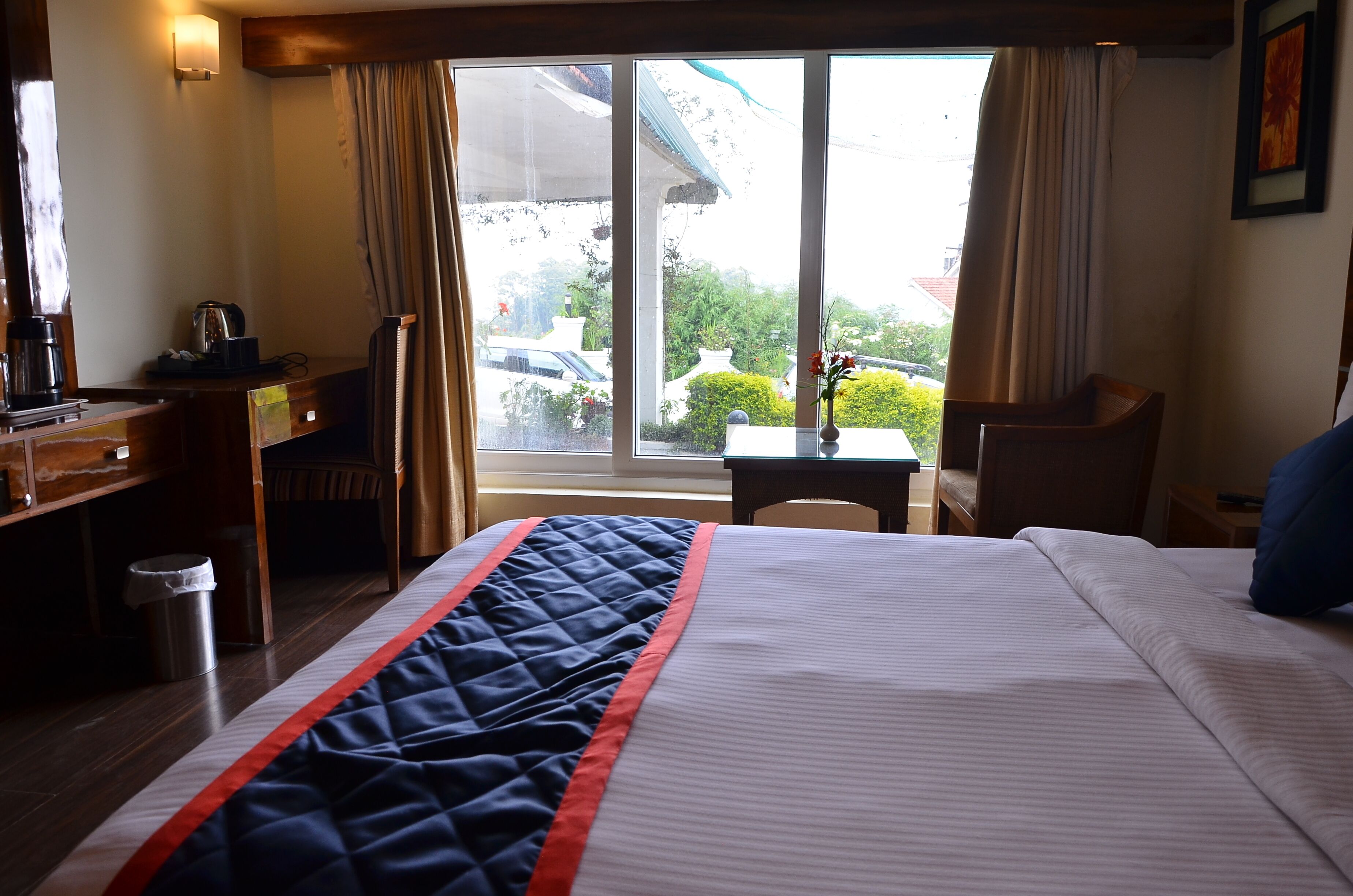A hotel room with a bed, a desk, a chair, a small table, and a window with a view of the outside.