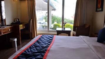 A hotel room with a bed, a desk, a chair, a small table, and a window with a view of the outside.