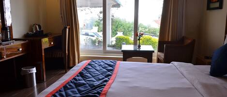 A hotel room with a bed, a desk, a chair, a small table, and a window with a view of the outside.