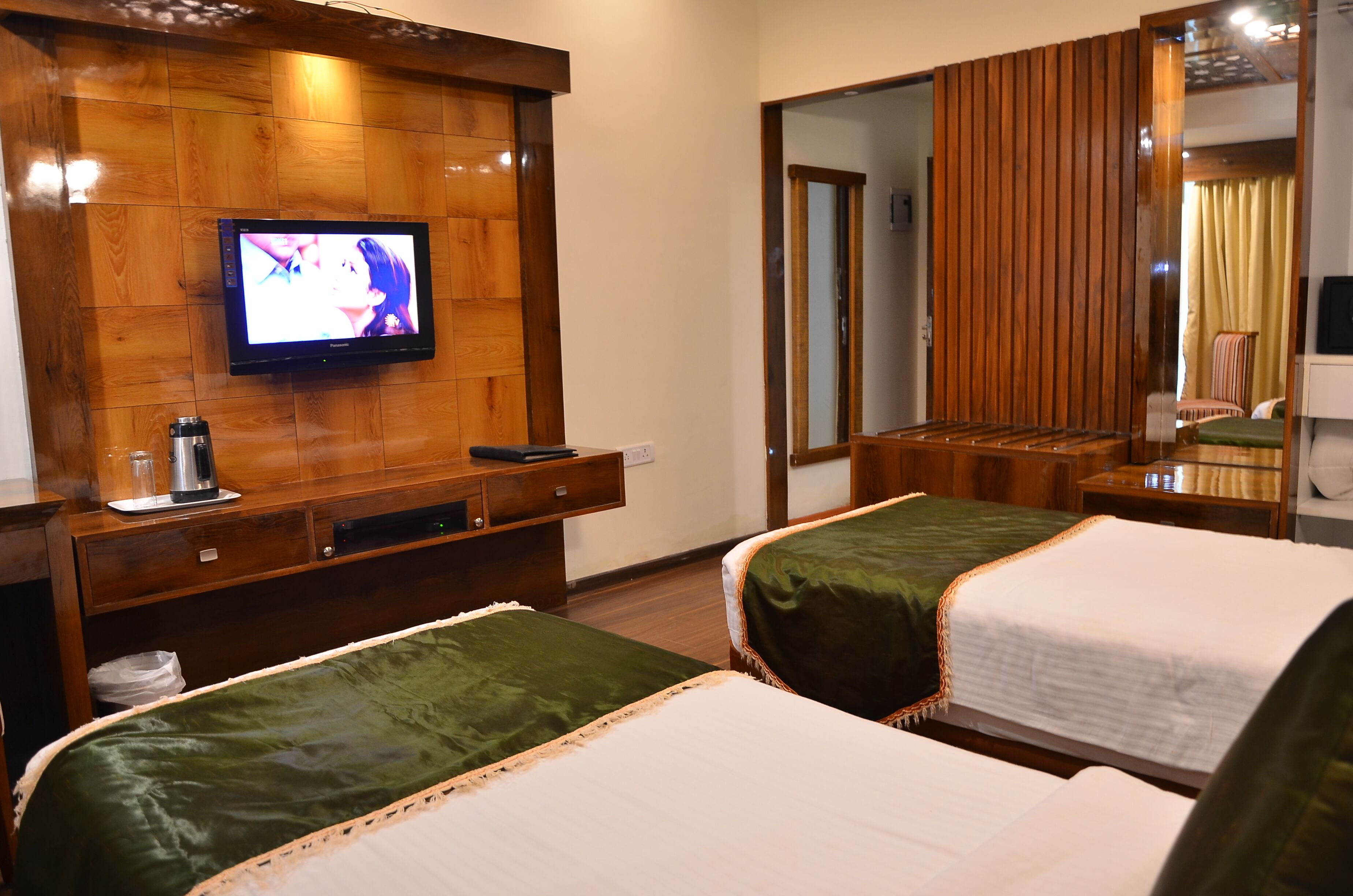 A hotel room with two beds, a TV mounted on a wooden wall, a mirror, and a wooden wardrobe.