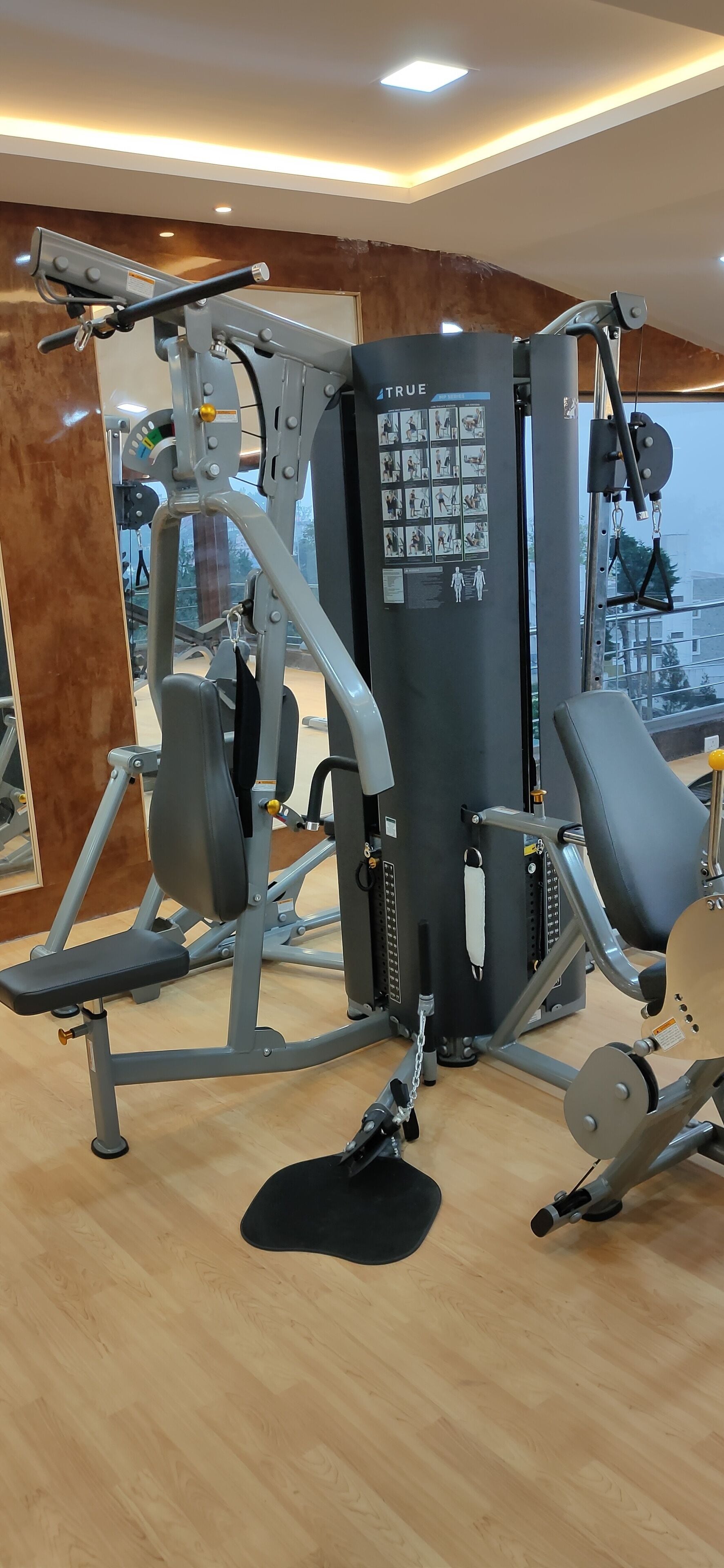 A gym with various exercise machines, a large mirror, and a view of the city through large windows.