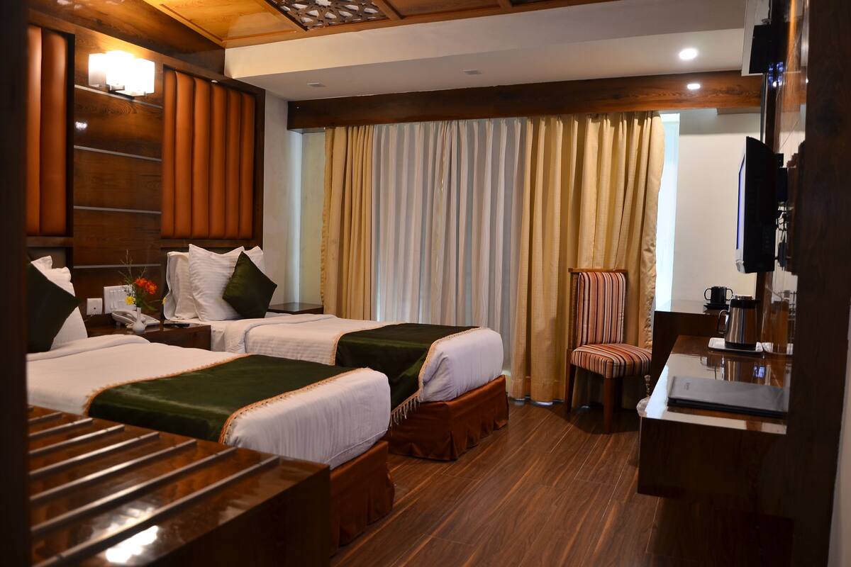 Habitación de hotel con dos camas, cabecero de madera, una mesita, una silla y un televisor.