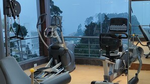 Ein Fitnessraum mit Trainingsgeräten, großen Fenstern und Holzboden.