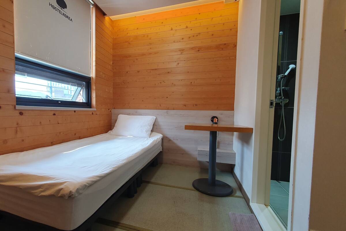 Una habitación pequeña con cama individual, paredes de madera y una ventana.