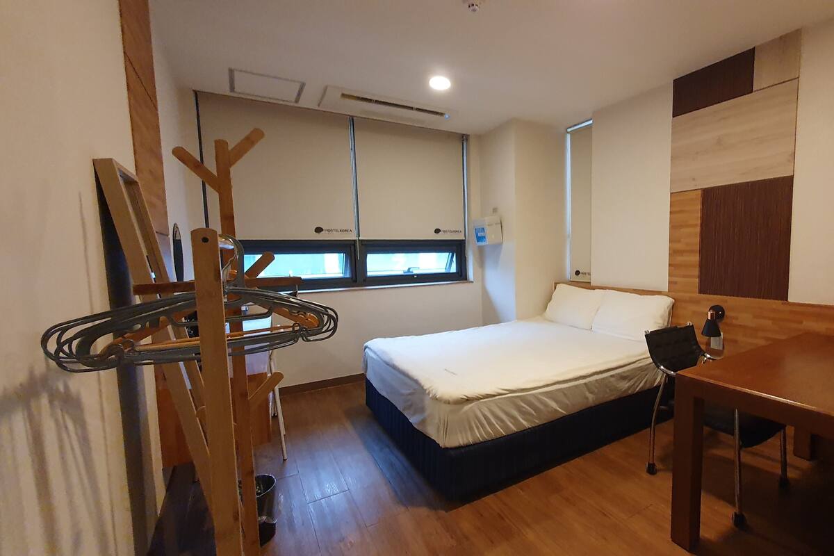Un dormitorio pequeño con cama, un escritorio de madera y ventana con vistas.