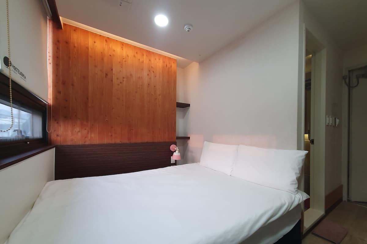 Una habitación de hotel moderna con una pared de acento de madera, una cama con ropa blanca y una mesita de noche con una lámpara rosa.