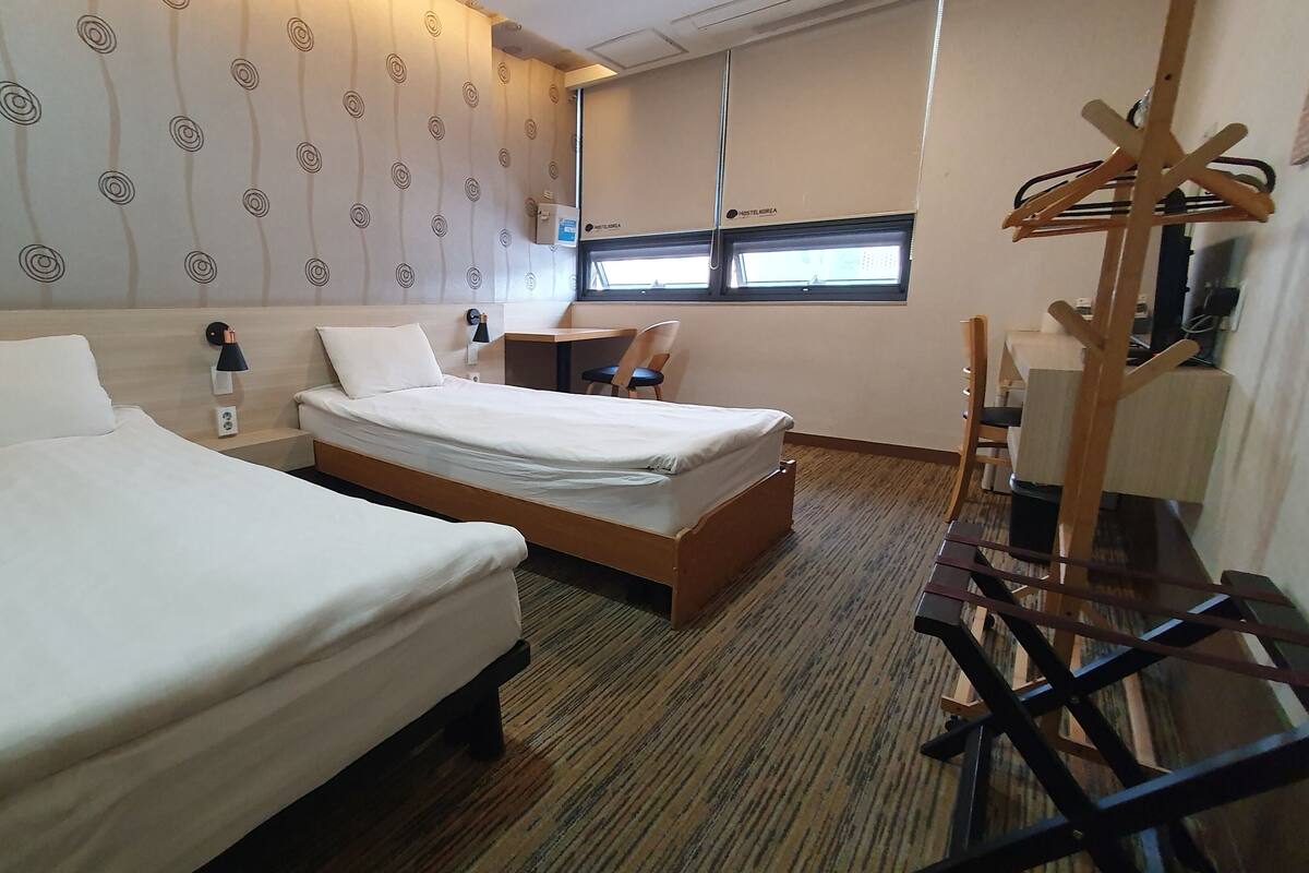 Habitación de hotel con dos camas, un escritorio, una silla, un televisor y una ventana.