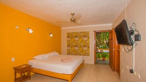 A bedroom with a bed, a ceiling fan, a wall-mounted TV, and a window with a view of greenery. - Koox City Garden Hotel (Playa del Carmen)