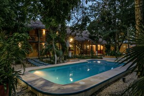 A pool area with a thatched-roof structure, surrounded by tropical plants and a small staircase leading to a building. - Koox City Garden Hotel (Playa del Carmen)