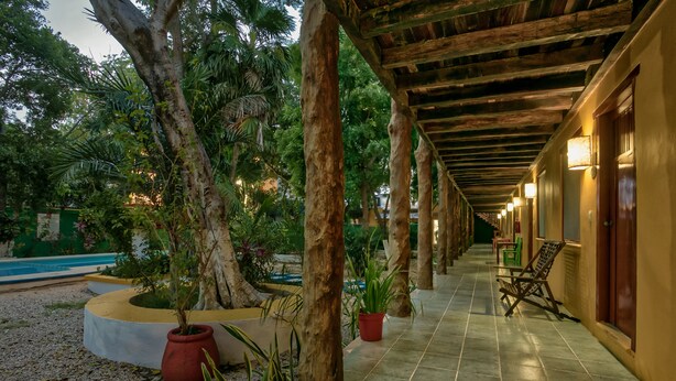 A covered walkway with potted plants and a pool in the background. - Koox City Garden Hotel (Playa del Carmen)