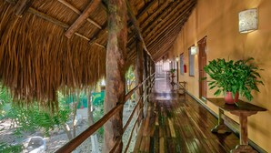 A corridor with a thatched roof, wooden floor, and a potted plant on a table. - Koox City Garden Hotel (Playa del Carmen)