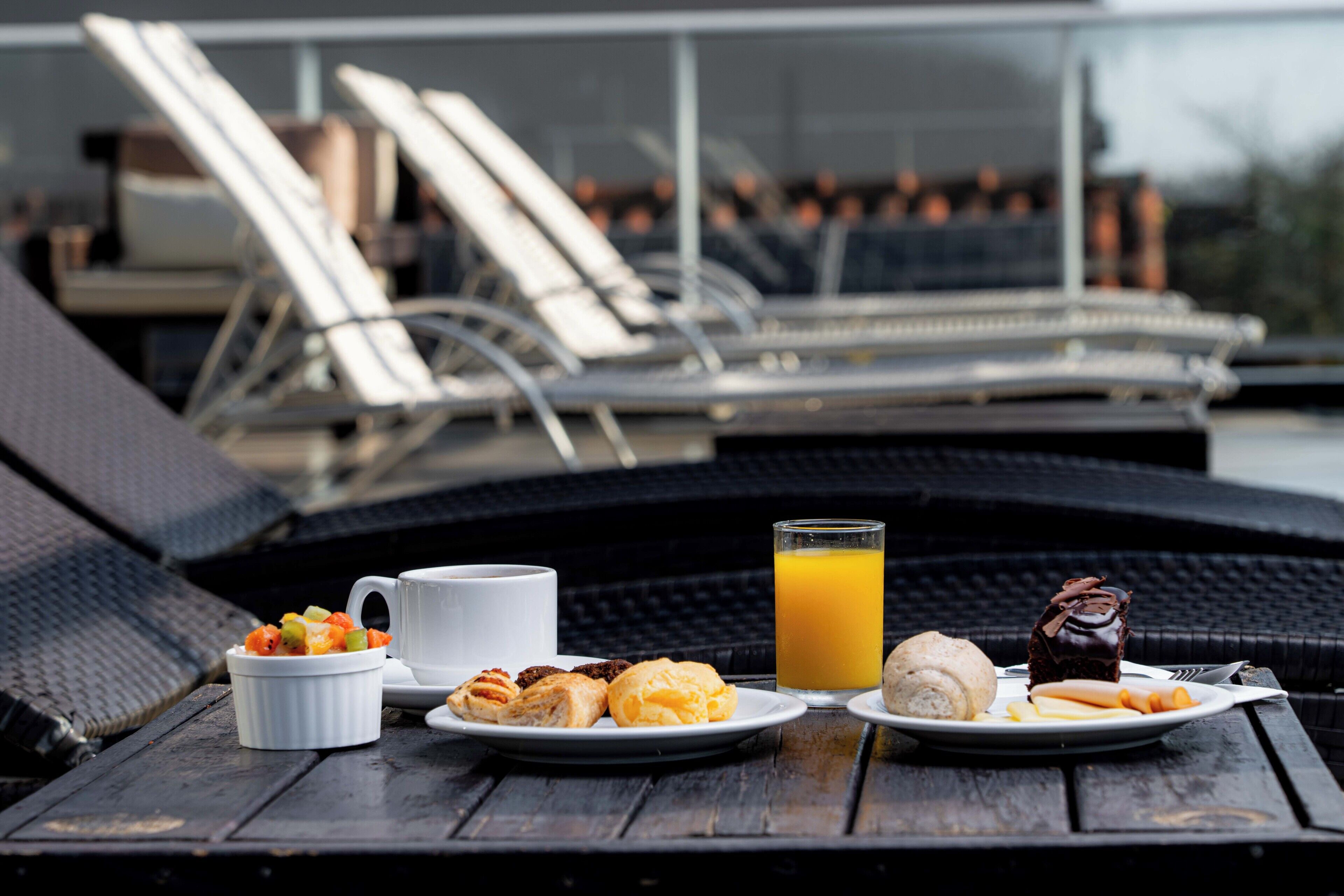 A breakfast setup on a wooden table with a white cup, a glass of orange juice, pastries, and a chocolate dessert.