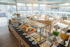 A buffet area with various food items and beverages, surrounded by tables and chairs. - Bossa Jurerê Hotel (Florianópolis)